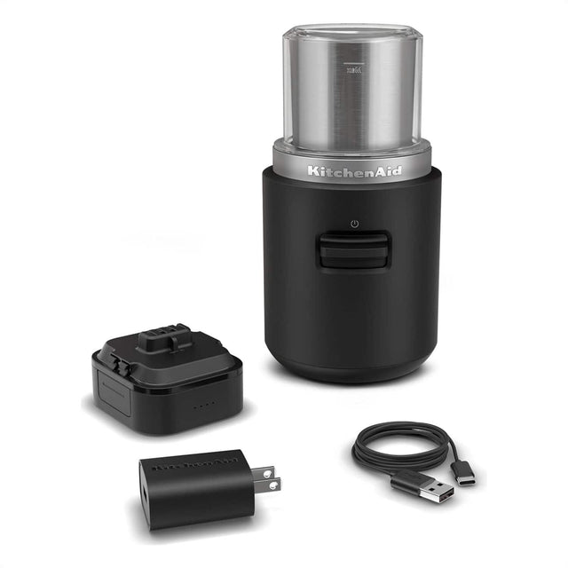 KitchenAid is a brand of kitchen appliances, including mixers and blenders. The image shows a black KitchenAid blender with a silver top, along with a black power adapter and a black cord. The blender is designed to be portable and easy to use, making it a convenient addition to any kitchen.